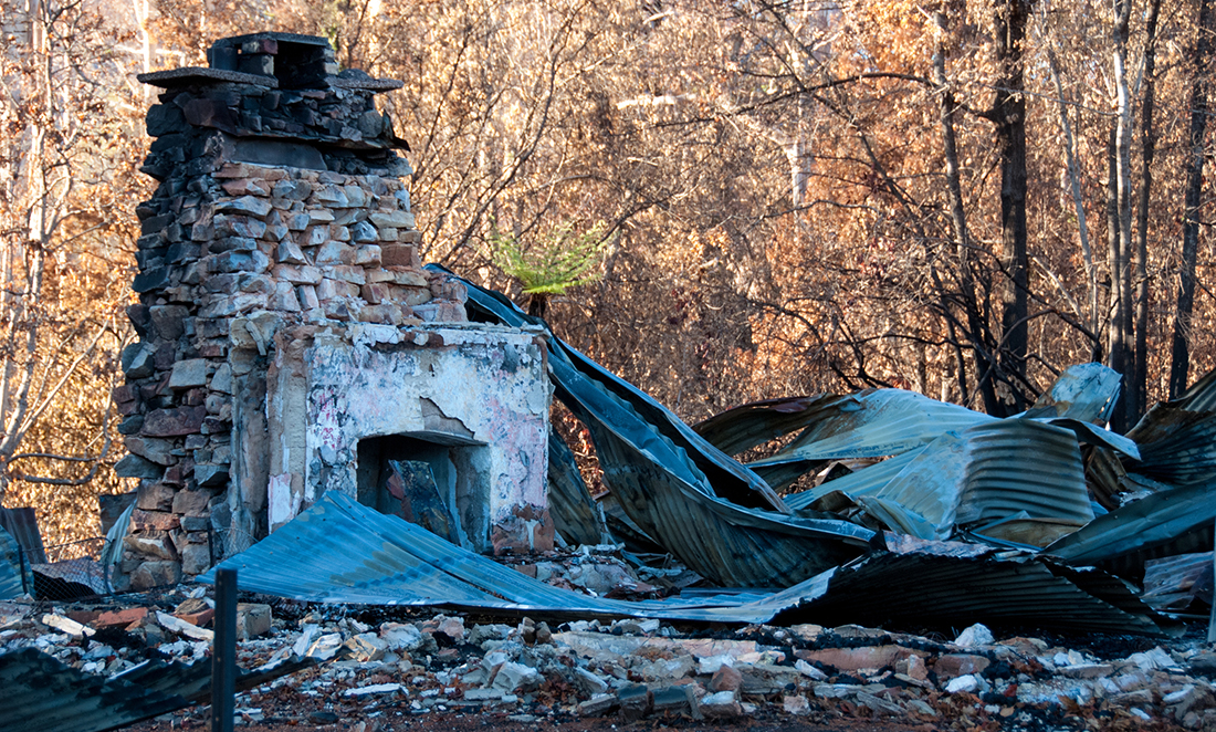 A brick fireplace remains standing amongst the burnt ruins of a house