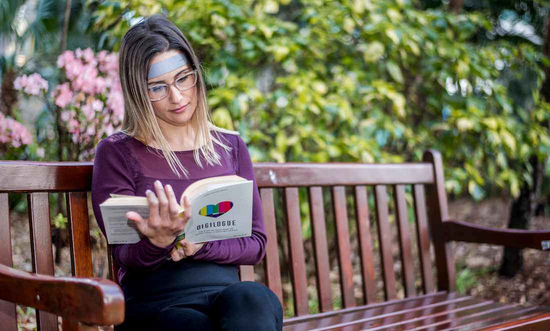 Lady reading a book on an outdoors bench, wearing a memory patch on her forehead