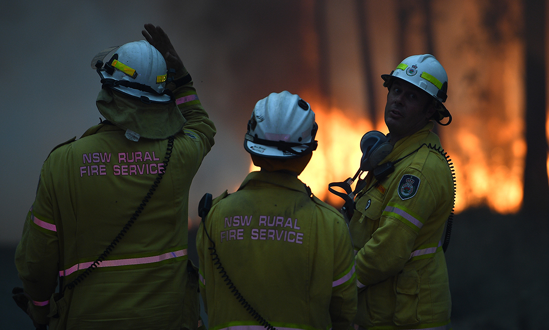 Three members of the NSW Rural Fire Service facing away from the camera review a fire in the distance