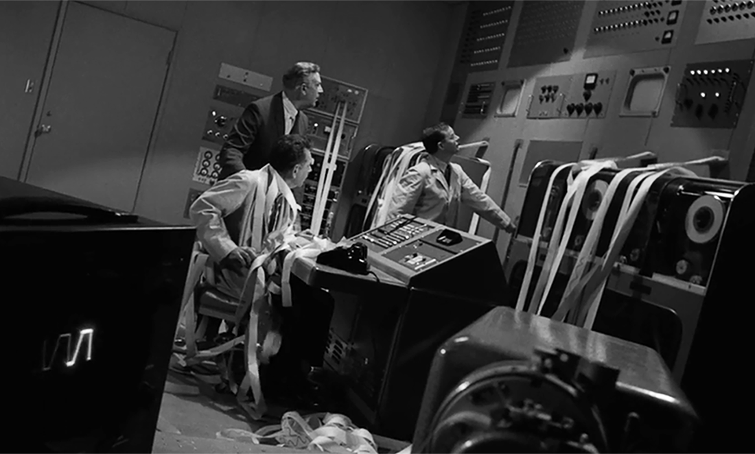 Black and white screen shot form The Twilight Zone (1964) showing a large computer room with lots of paper tape coming out of the machine