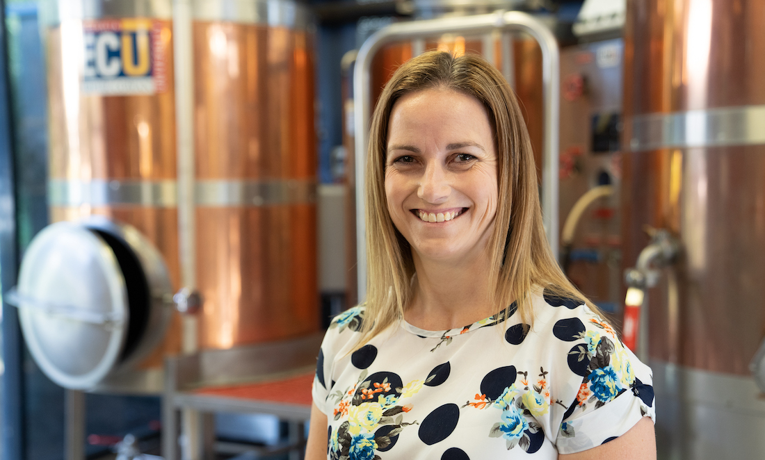 Professor Michelle Colgrave stands in front of beer brewing vats