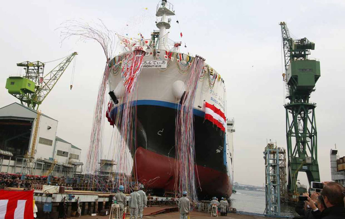 A large ship that will carry liquefied hydrogen berths at a dock with coloured launch streamers hanging over the hull