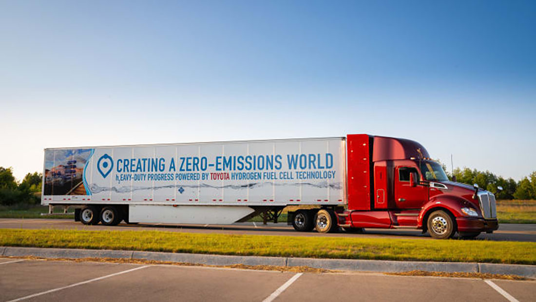 Long Toyota Fuel Cell Truck with a red cabin and a poster on the trailer that reads: Creating a Zero-emissions world"