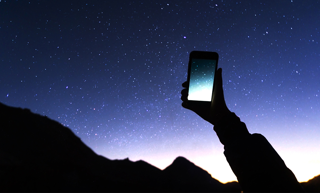 Hand holding a smartphone up to the night sky.