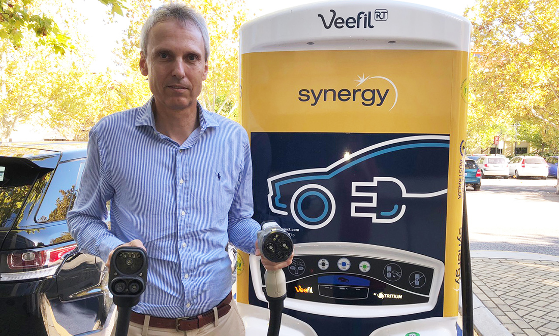 Man stands in front of an EV charging station at UWA holding the chargers
