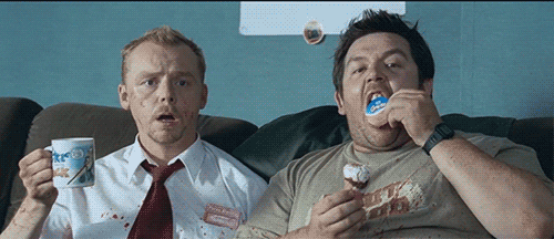 Movie still from Shaun of the Dead showing the 2 main characters sitting on a couch; one drinking a cup of tea and the other eating a Cornetto icecream