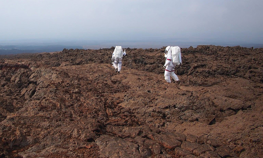 Two people in astronaut suits walk across the terrain in Hawai'i on Mars training missions