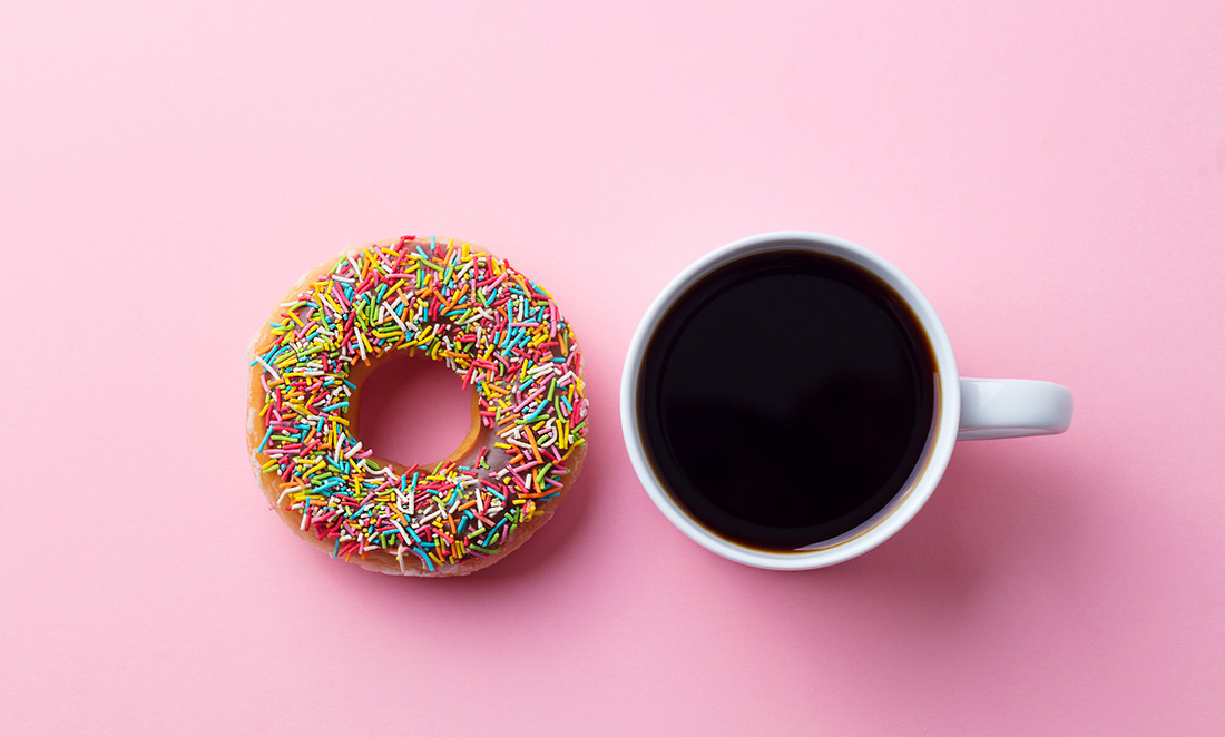 Coffee with donut on pink paper background.