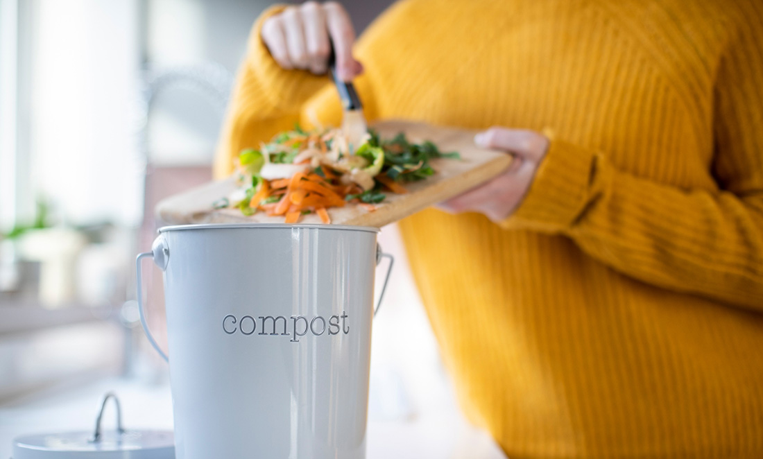 Woman scraping leftover vegetables into a small bin marked 'Compost'
