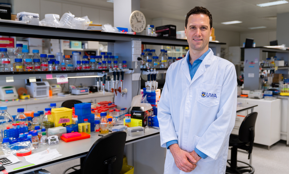 Professor Ryan Lister in a science lab, wearing a lab coat with 'UWA' on the pocket