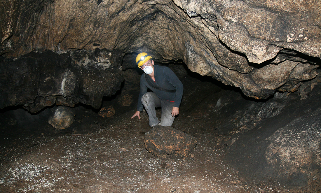 Professor Morten Allentoft in an underground cave in Armenia, wearing a yellow hardhat and a white facemask. He is looking for Neanderthal skeletons
