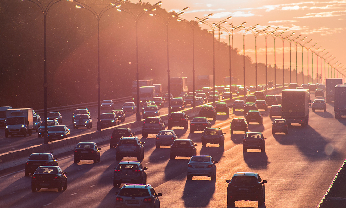 Rows of cars driving along a freeway against a dusky orange sky