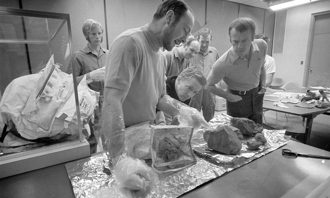 Six men stand around a table of melon-sized rocks, as the Apollo 14 crew men show off some of the largest of the lunar rocks which they brought back from the Moon in 1971