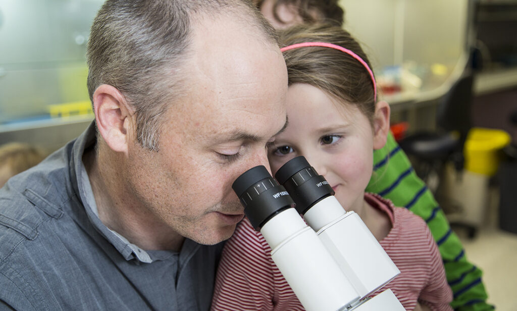 David Elliot looking into microscope with a young girl watching