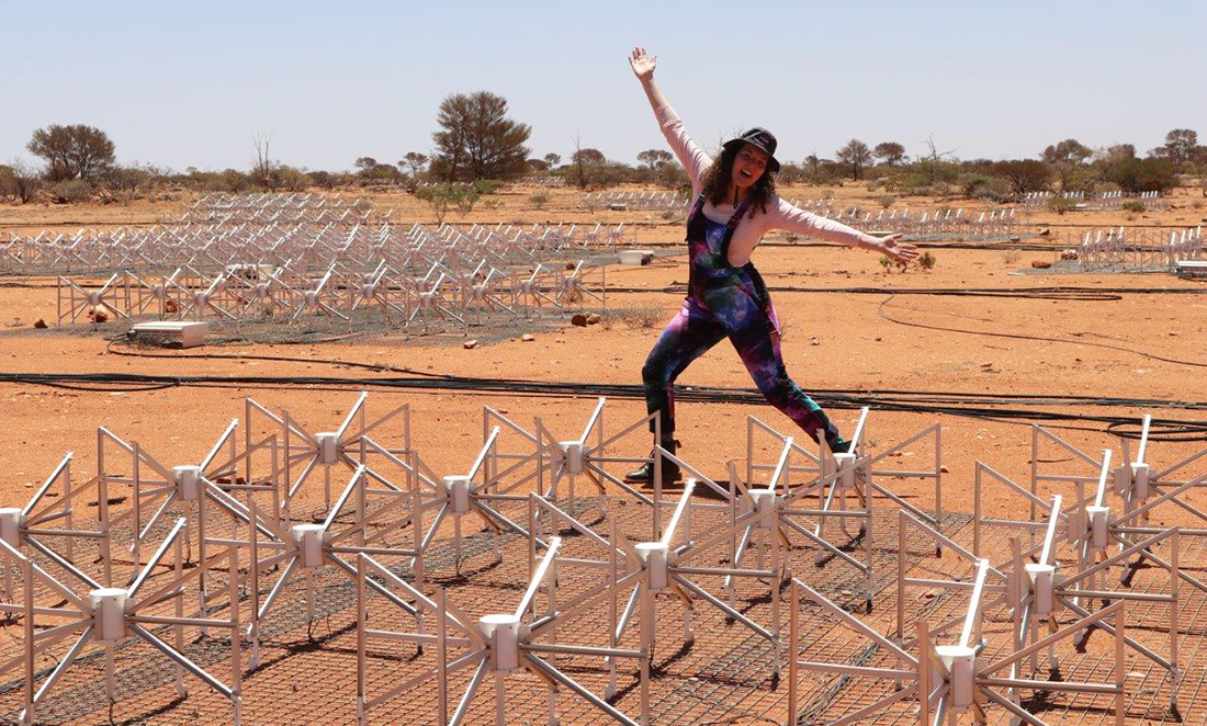 Astronomer Kathryn Ross poses at the Murchison Widefield Array (MWA), hundreds of white antennas stand on red sand