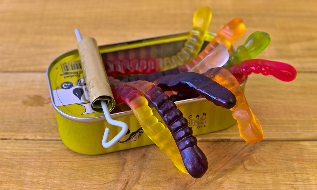 An open sardine tin is overflowing with colourful gummy worms, showing 'a can of worms'
