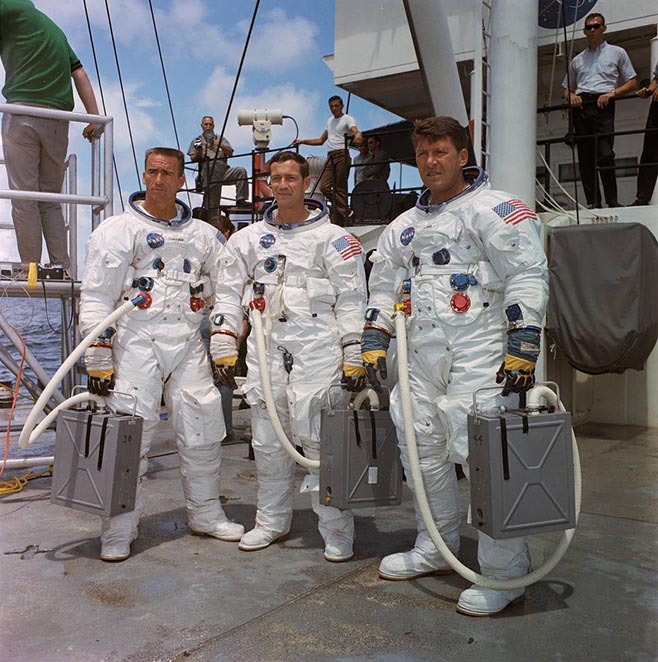 Three NASA astronauts wearing white space suits pose for the camera - they are the crew members of the Apollo 7 mission