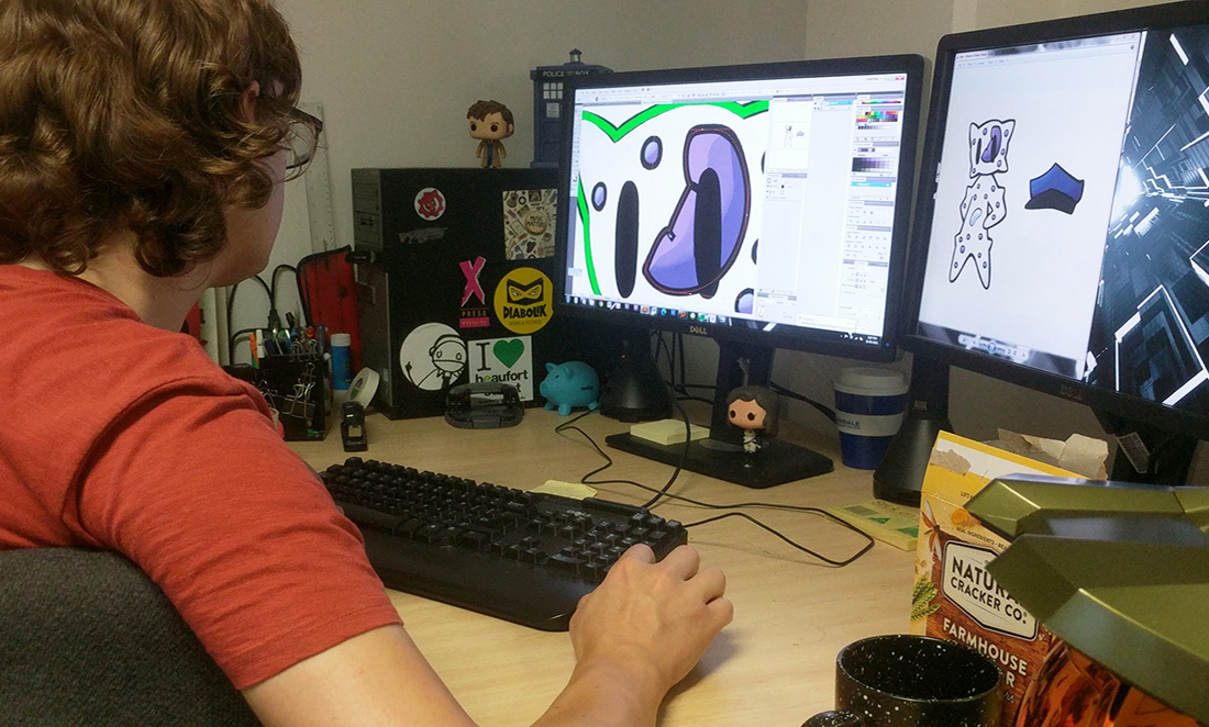 Shown from behind, MicroToons artist Sam bworks on his computer. A purple illustration is shown on his screen.