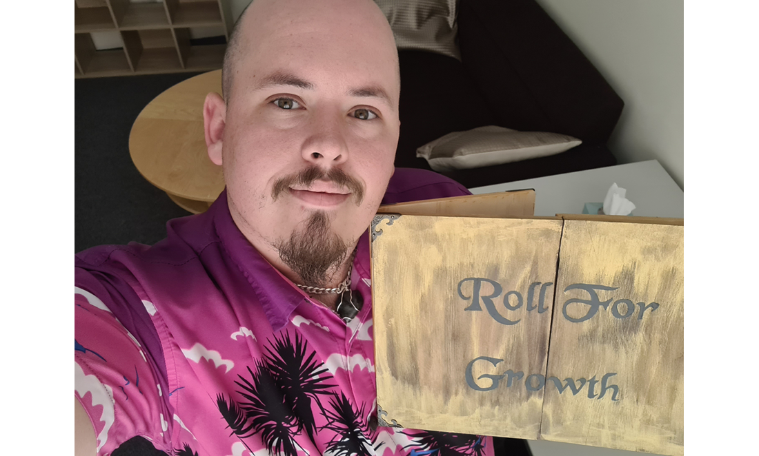 Michael Keady holds up a game master screen that reads 'Roll for Growth'