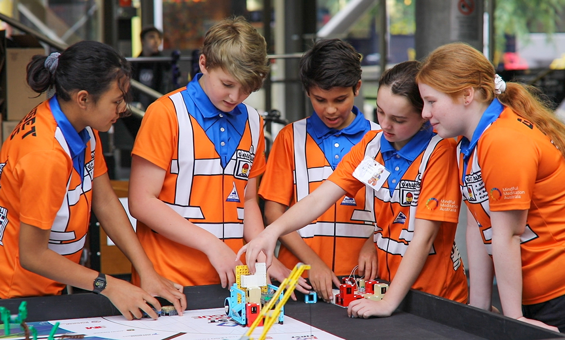 A group of five students look down at a robot they are making as part of the FIRST LEGO League WA