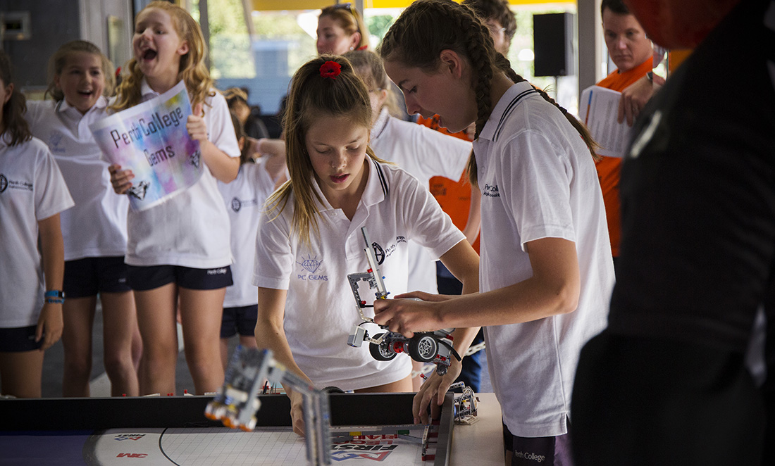 Two female students in white t-shirts work together to build a LEGO robot