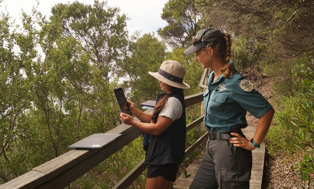 A park ranger watches a young girl photogrpah the bush on an iPad along the Cape Conran trail