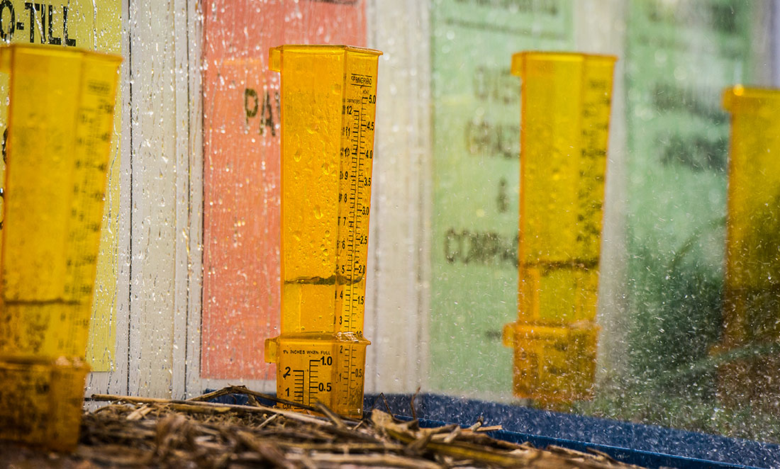 Four orange test tubes are set up on soil to test nutrient quality