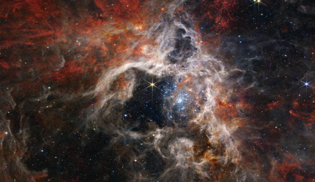 Image: It’s only fitting to show an image of (part of) the Tarantula Nebula taken by the James Webb (hah!) Space Telescope. Note the dense core of new blue stars (right of centre) and the surrounding large voids relatively clear of gas, before reaching the wispy exterior of ionised hydrogen blown out of the centre of the region by the hot, new stars. Credit: NASA, ESA, CSA, STScI, Webb ERO Production Team  